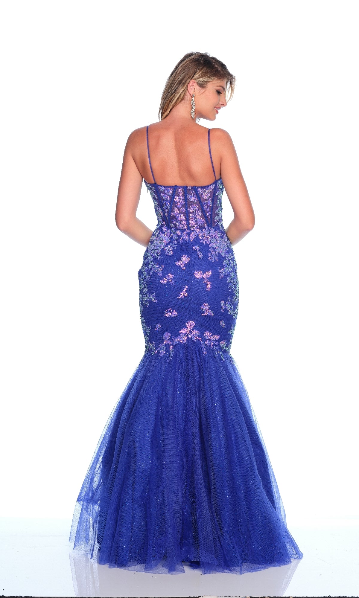 A woman in the Dave & Johnny 12134 blue mermaid prom dress with floral embroidery, thin straps, and sequin details poses with her back to the camera against a white background.